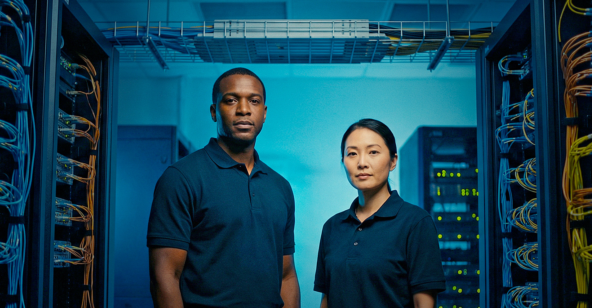 Two workers stand in a server room that is part of a hyper-scale data center.